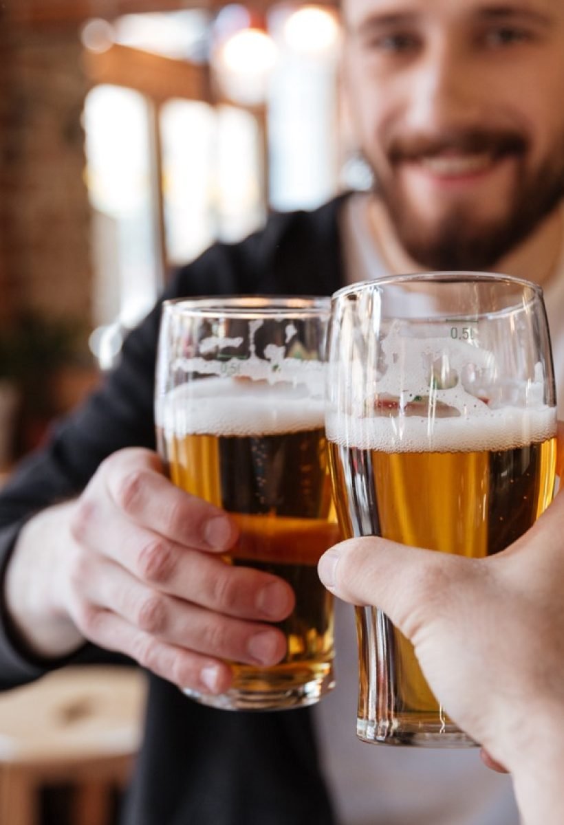 First view of man clinking glasses with friend on bar. Focus on cups.